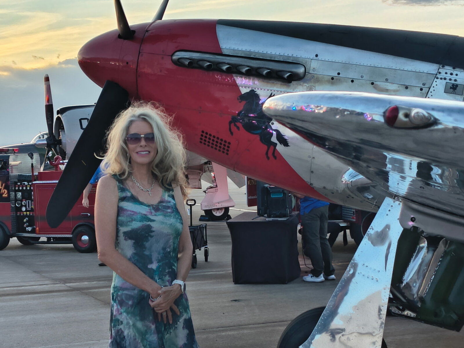 Laura Cavey on the tarmac at sunset beside a red-nosed P-51 Mustang at the Douglas County Heroes Gala, Signature Aviation, Centennial Airport
