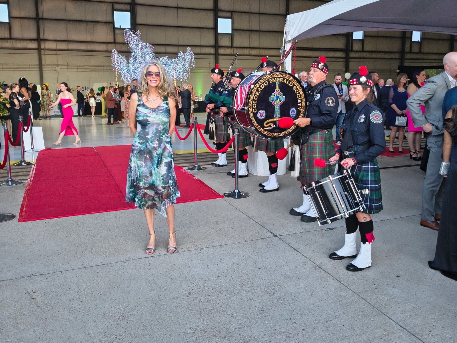 Laura Cavey on the red carpet inside the hangar as the Colorado Emerald Society pipes and drums, in kilts and police uniforms, play beside her