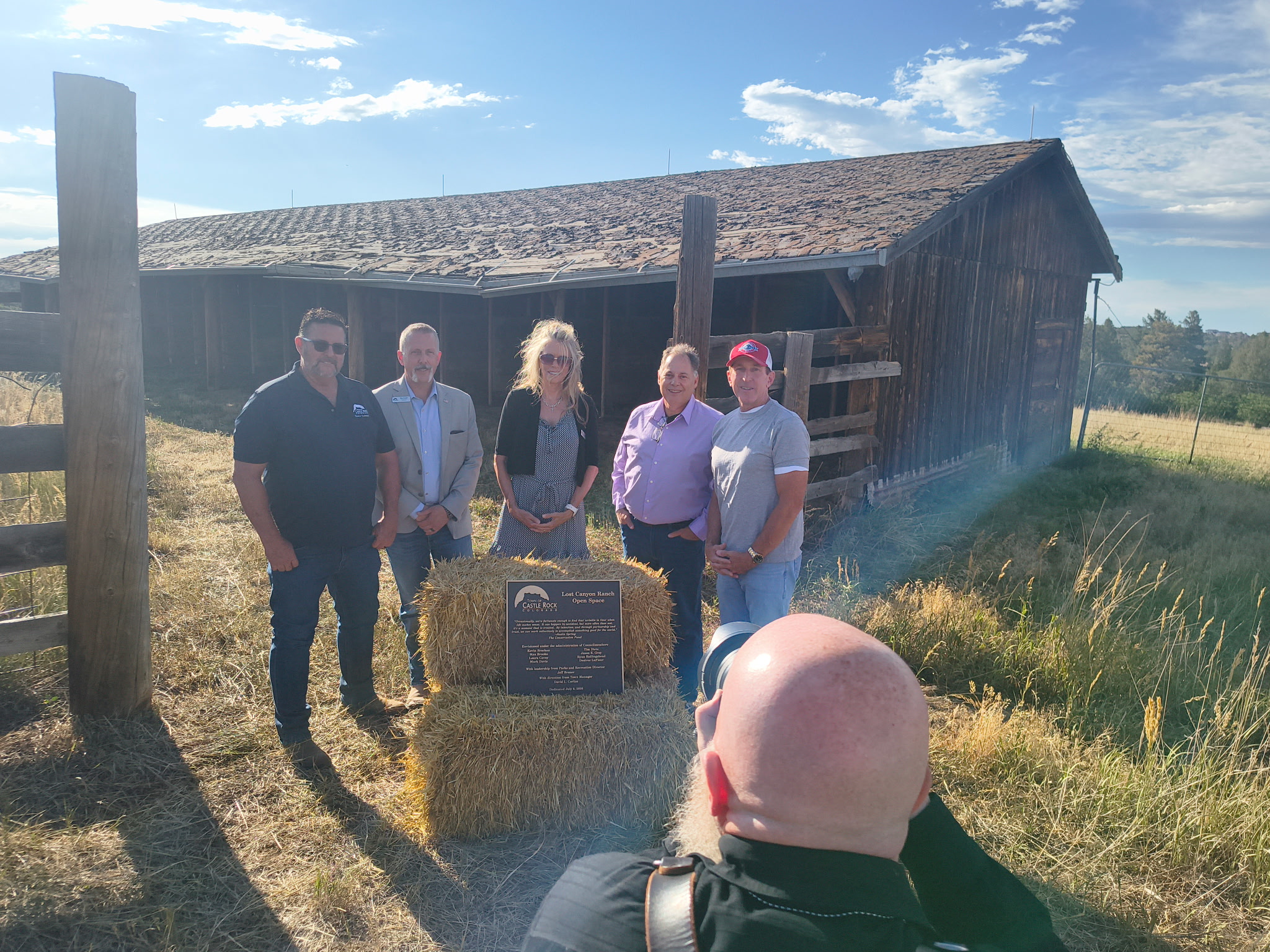 Laura Cavey and fellow Castle Rock Town Councilmembers at the Lost Canyon Ranch Open Space plaque dedication, gathered around the bronze plaque on hay bales in front of the historic ranch barn